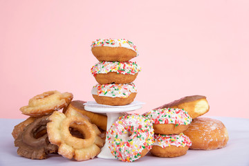 Cake donuts with white frosting and colorful sprinkles stacked on and around a small pedestal surrounded by birthday presents. Number 1 candle burning for first birthday party.