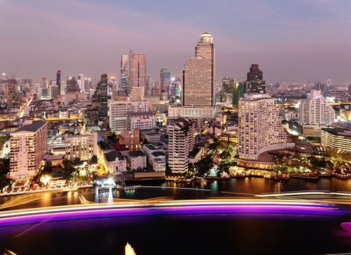Night cityscape of Bangkok in bird's eye view ~ Aerial panorama of Bangkok in evening twilight, with busy light trails of boats & ships on Chao Phraya River and modern skyscrapers by the riverside