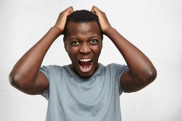 Portrait of desperate annoyed black male screaming in rage and anger tearing his hair out while feeling furious and mad with something. Negative human face expressions, emotions and feelings