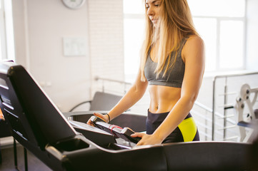 young woman is engaged fitness in gym. Performs cardio load on treadmill, running and walking with acceleration. sport, fit, lifestyle, technology and people concept