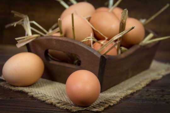Chicken eggs with straw in wooden bowl on wooden background