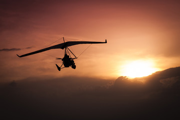 Fototapeta na wymiar Weight-Shift ultralight aircraft silhouette in the sunset, above stormy clouds