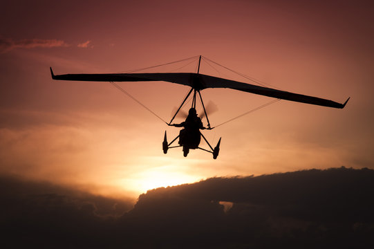 Weight-Shift ultralight aircraft silhouette  in the sunset, above stormy clouds