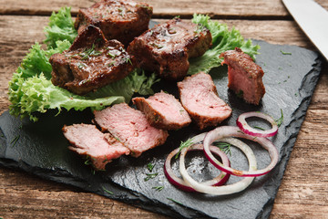 Tasty shashlik decorated with lettuce leaves and onion rings on black plate, close up view. Restaurant menu photo.