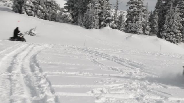 Two people riding snowmobiles through fresh snow on Mt Hood in Oregon.