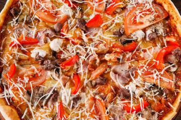 Appetizing and delicious fresh baked colorful pizza with mushrooms, bacon, chicken, paprika and tomato, close up. Italian cuisine, traditional fast food.