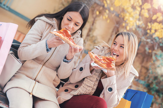 Friends eating pizza. Two young women eating pizza after shopping. Lifestyle, consumerism, modern life