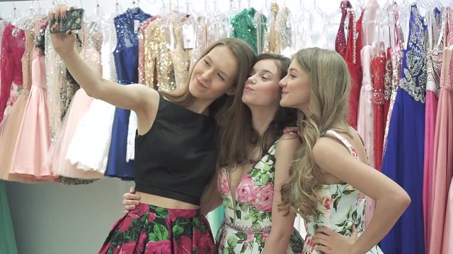 Attractive girls posing on the mobile phone camera and making selfies in the showroom of the shopping center