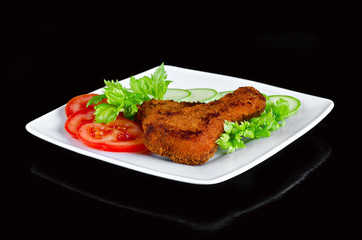 Chicken meat, breaded and fried with fresh vegetables and white plate and black background
