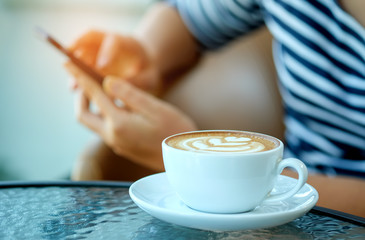 Women playing smart phone with coffee heart latte in hand put on the legs.