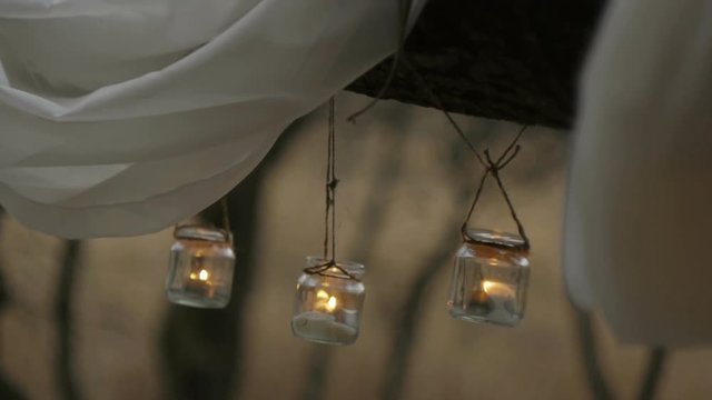 candles lit in a glass jar suspended on a rope or twine