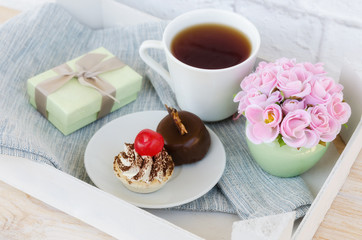 Fototapeta na wymiar Cup of tea with cute sweet cakes, roses and box gift on wooden tray. Woman morning, breakfast concept.