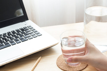 beautiful female's hand holding a glass of water with messy desk