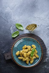 Above view of italian traditional gnocchi with basil pesto, grey stone background with copyspace