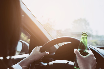 Woman holding beer bottle while driving a car