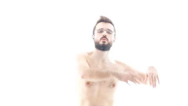 Dynamic bearded naked man dancing and listening contemporary music on earphones, hi-key studio isolated on white background.