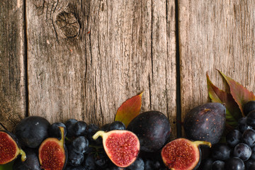 Figs halves with grape on wood flat lay. Top view on rustic wooden background with ripe autumn purple fruits border, free space. Harvest, fall, gourmet concept