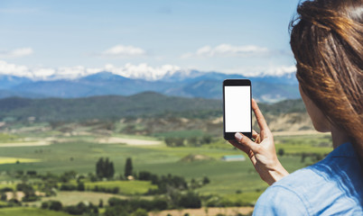 Hipster photograph on smart phone gadget mobile, mock up of blank screen. Girl traveler hold in hand mobile on background mountain landscape horizon. Tourist look map on trip, lifestyle concept