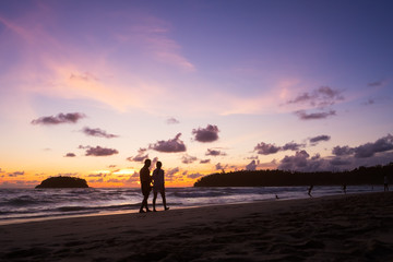 Couple walking on the beach at sunset.