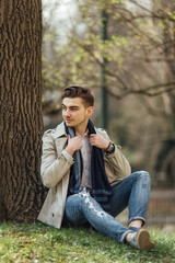 Fashionable man sitting near trees with blur background