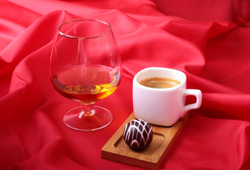 White cup of coffee and cognac in a glasses, pralines on red background.