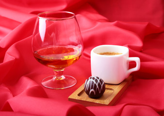 White cup of coffee and cognac in a glasses, pralines on red background.