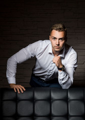 Young handsome businessman relies on leather couch in confident pose