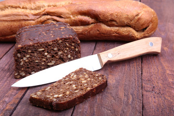 Assorted fresh breads, slice and knife isolated on old wood table.