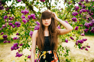 Laughing and smiling beautiful  happy artistic young model girl with long hair in summer lilac garden with flowers posing for camera. Spring concept.