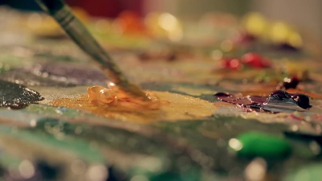The artist mixes oil orange paint on a palette close up