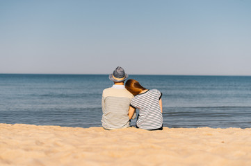 young lovers sitting together on a beach sand beside a sea in summer sunny day and looking to the horizon