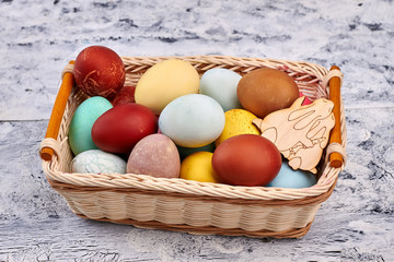 Basket with colored Easter eggs. Wicker basket, painted wood background.
