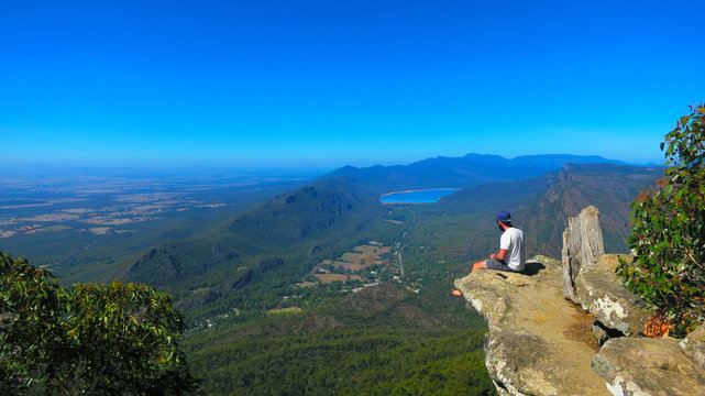 Adventurous young man sitting on a height cliff edge at the top of the Boroka Lookout at the The Grampians National Park (Gariwerd), Victoria, Australia