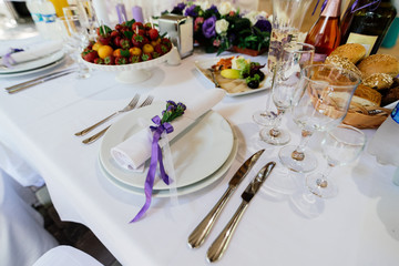 White napkin with purple flowers on a white empty plate on a dining table. Table setting. Table served for edding dinner, close up view