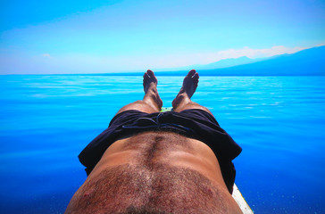 Head Cam body photo - POV of a young man relaxing sun bathing on his paddle board in calm still tropical north Bali waters during sunrise hours