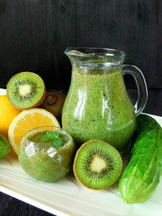Green smoothie made of spinach, kiwi, cucumber, lemon and mint in different glass vessels for healthy nutrition