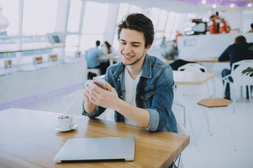 Attractive young man or freelancer with mobile is sitting in cafe and drinking coffee