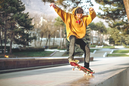 The teenager in a sweatshirt and a cap jumps with a board in the city against the backdrop of the urban sunset light. Photo of extreme