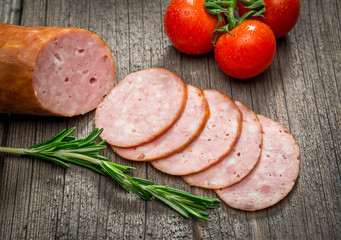 Salami sausages sliced with pepper, garlic and rosemary on cutting board on wooden table. Top view