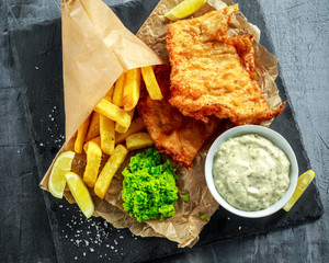 British Traditional Fish and chips with mashed peas, tartar sauce on crumpled paper.