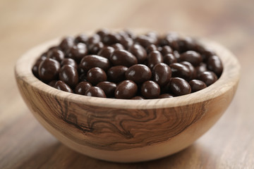 small chocolate dragee in wood bowl on table, coffee beans or pine seeds