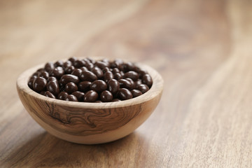 small chocolate dragee in wood bowl on table, coffee beans or pine seeds