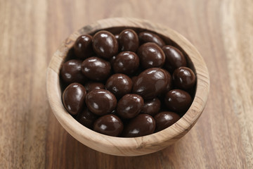 chocolate covered almonds in wood bowl on table, closeup