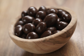 chocolate covered almonds in wood bowl on table, closeup