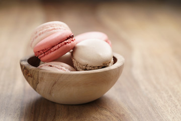 pastel colored macarons with strawberry, rose and caramel flavour in wood bowl with copy space