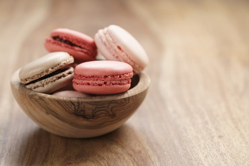 Obraz na płótnie Canvas pastel colored macarons with strawberry, rose and caramel flavour in wood bowl with copy space