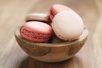 pastel colored macarons with strawberry, rose and caramel flavour in wood bowl on table