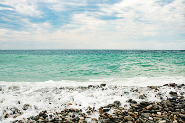 Fototapeta na wymiar Beach with pebbles, sea with waves and sea foam.
