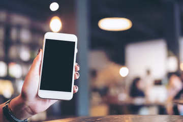 Mockup image of hand holding white mobile phone with blank black screen in cafe