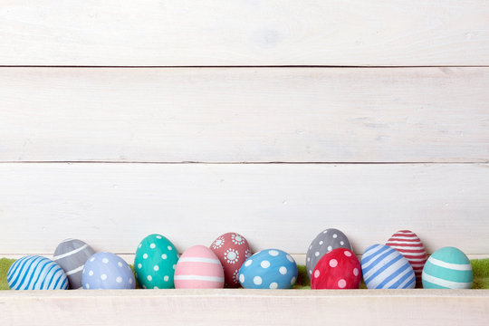 Twelve colorful handmade Easter eggs stand in a row on a white wooden background with space from above